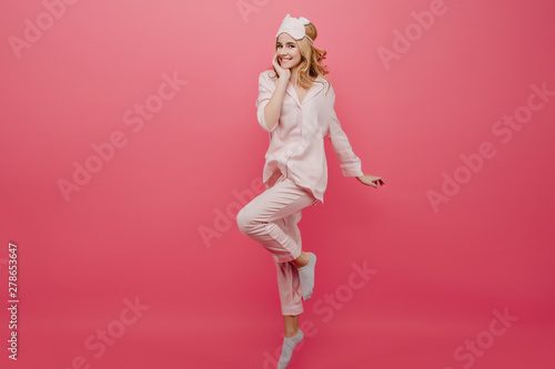 Full-length portrait of winsome girl in pajamas and socks dancing on pink background. Studio shot of graceful caucasian female lady in eyemask having fun in morning.