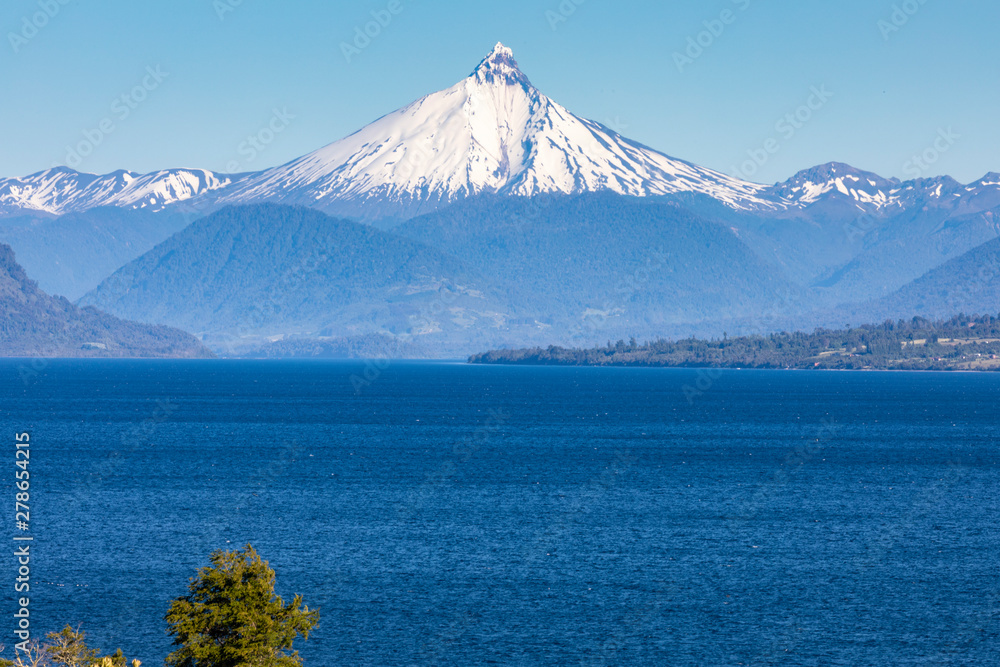 The amazing Puntiagudo Volcano above the waters of Rupanco Lake, the tress inside the forest and the clouds making it an awesome volcanic landscape. A sharpen snow capped summit. South of Chile.
