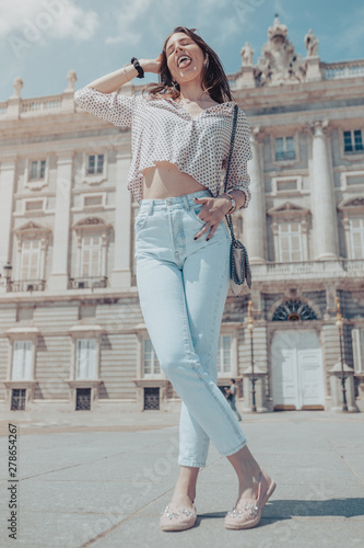 Beautiful young woman posing and sticking out tongue near Royal Palace of Madrid, Spain © EGHStock
