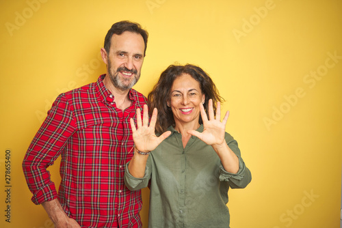 Beautiful middle age couple over isolated yellow background showing and pointing up with fingers number ten while smiling confident and happy.
