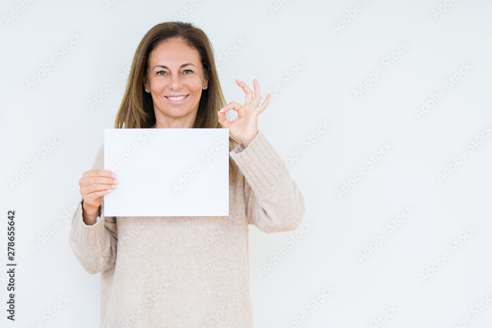 Middle age woman holding blank paper sheet over isolated background doing ok sign with fingers, excellent symbol Middle age woman holding blank paper sheet over isolated background doing ok sign with fingers, excellent symbol