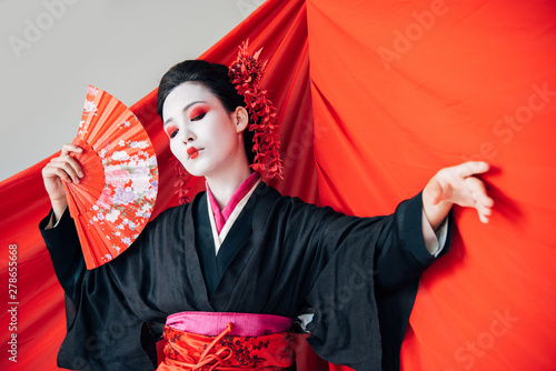 Foto beautiful geisha in black kimono with hand fan and red cloth on background danci