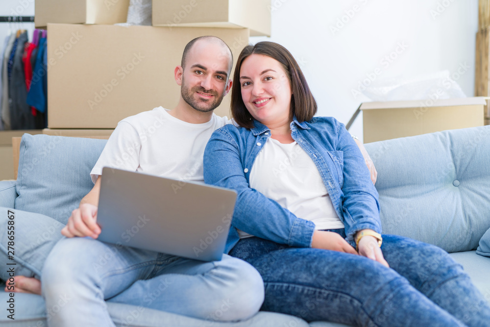 Young couple sitting on the sofa at new home using computer laptop, smiling happy for moving to a new apartment