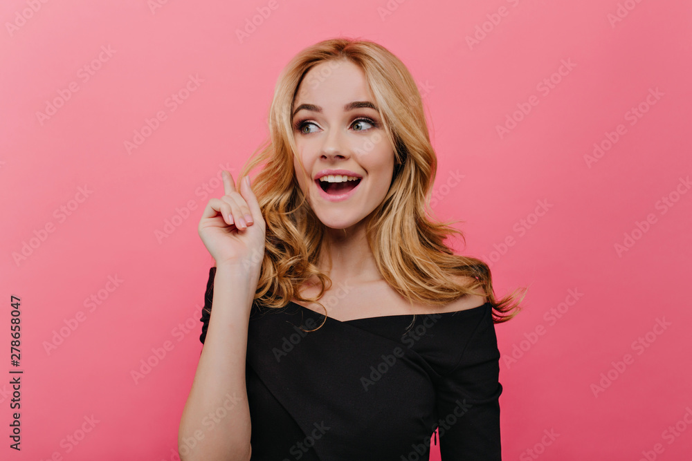 Winsome fair-haired woman posing in studio with surprised smile. Indoor photo of white interested girl in black dress isolated on pink background. Winsome fair-haired woman posing in studio with surprised smile. Indoor photo of white interested girl in black dress isolated on pink background.