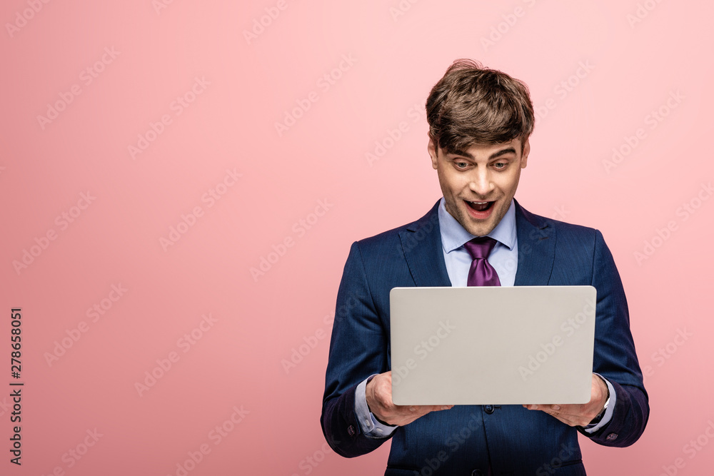 cheerful businessman in formal wear looking at laptop on pink background cheerful businessman in formal wear looking at laptop on pink background