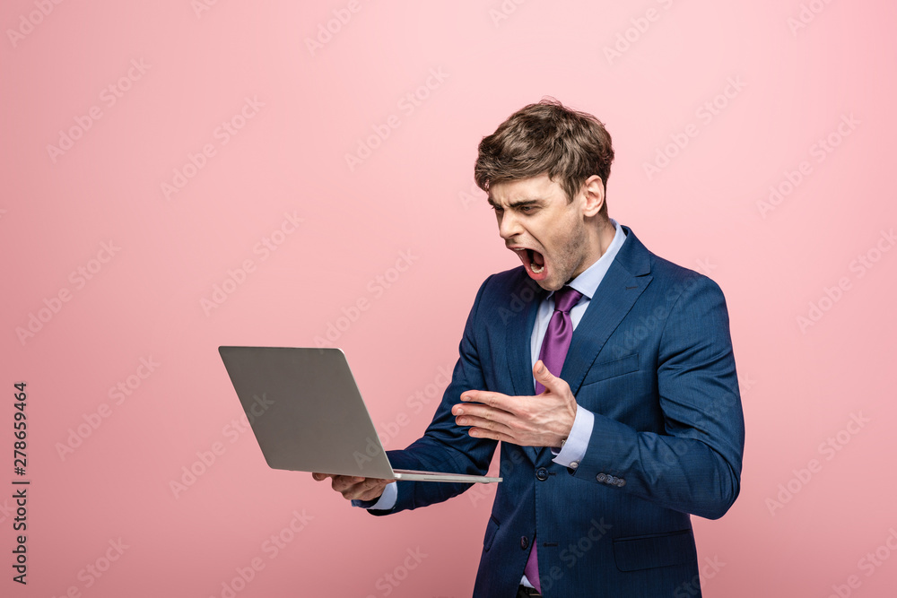 angry businessman quarreling while looking at laptop isolated on pink angry businessman quarreling while looking at laptop isolated on pink