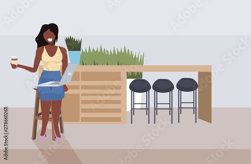 businesswoman sitting at counter desk african american girl using laptop and drinking coffee modern cafe interior flat horizontal full length