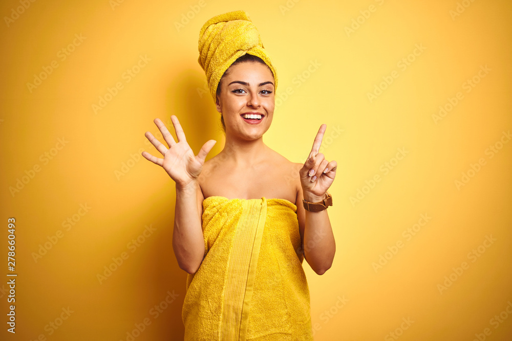 Young beautiful woman wearing towel after shower over isolated yellow background showing and pointing up with fingers number six while smiling confident and happy. Young beautiful woman wearing towel after shower over isolated yellow background showing and pointing up with fingers number six while smiling confident and happy.