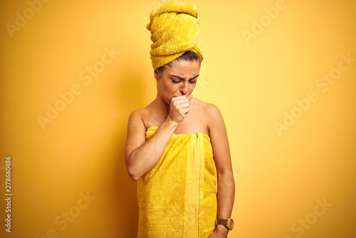 Young beautiful woman wearing towel after shower over isolated yellow background feeling unwell and coughing as symptom for cold or bronchitis. Healthcare concept.