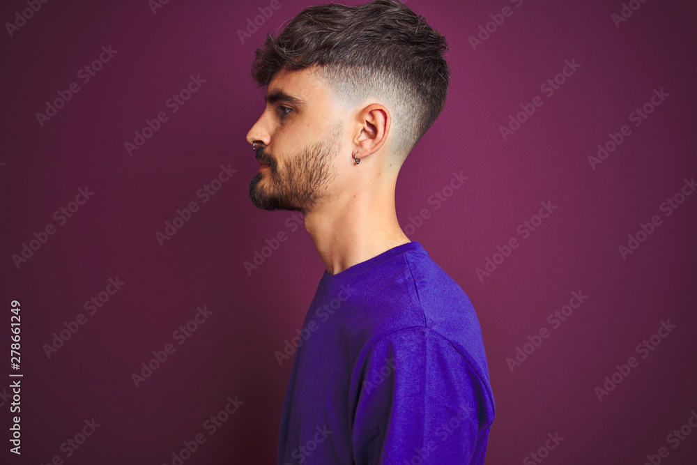 Young man with tattoo wearing t-shirt standing over isolated purple background looking to side, relax profile pose with natural face with confident smile. Young man with tattoo wearing t-shirt standing over isolated purple background looking to side, relax profile pose with natural face with confident smile.