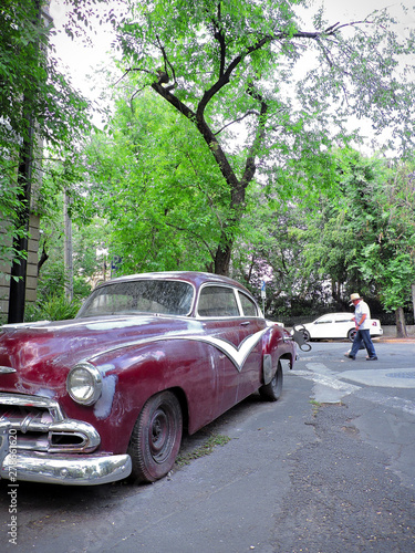 An old red car parked in the street seen in perspective.