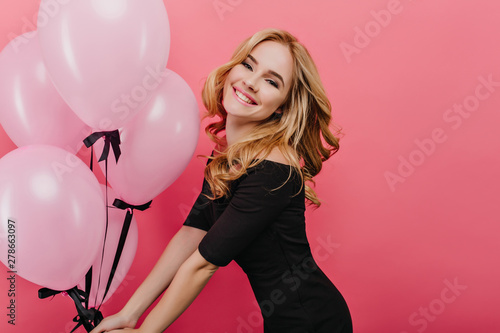 Slim white woman with curly hairstyle celebrating her birthday and happy laughing. Indoor photo of cheerful caucasian girl dancing on pink background in holiday.