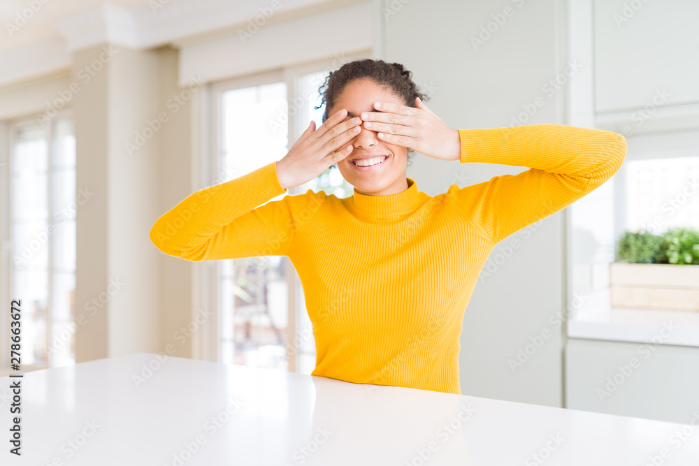 Beautiful african american woman with afro hair wearing a casual yellow sweater covering eyes with hands smiling cheerful and funny. Blind concept. Beautiful african american woman with afro hair wearing a casual yellow sweater covering eyes with hands smiling cheerful and funny. Blind concept.