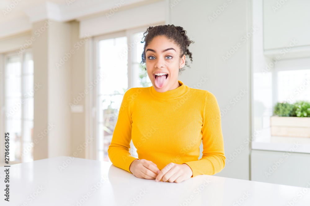 Beautiful african american woman with afro hair wearing a casual yellow sweater sticking tongue out happy with funny expression. Emotion concept. Beautiful african american woman with afro hair wearing a casual yellow sweater sticking tongue out happy with funny expression. Emotion concept.