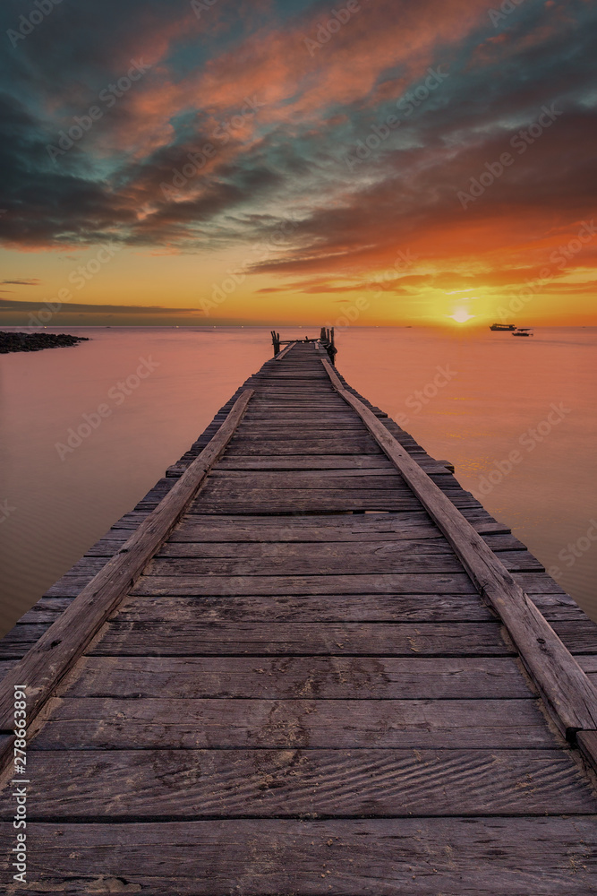 Old wooden pier stretching out into the sea with a dramatic sunset.