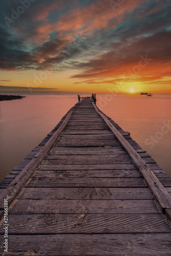 Fototapeta Naklejka Na Ścianę i Meble -  Old wooden pier stretching out into the sea with a dramatic sunset.