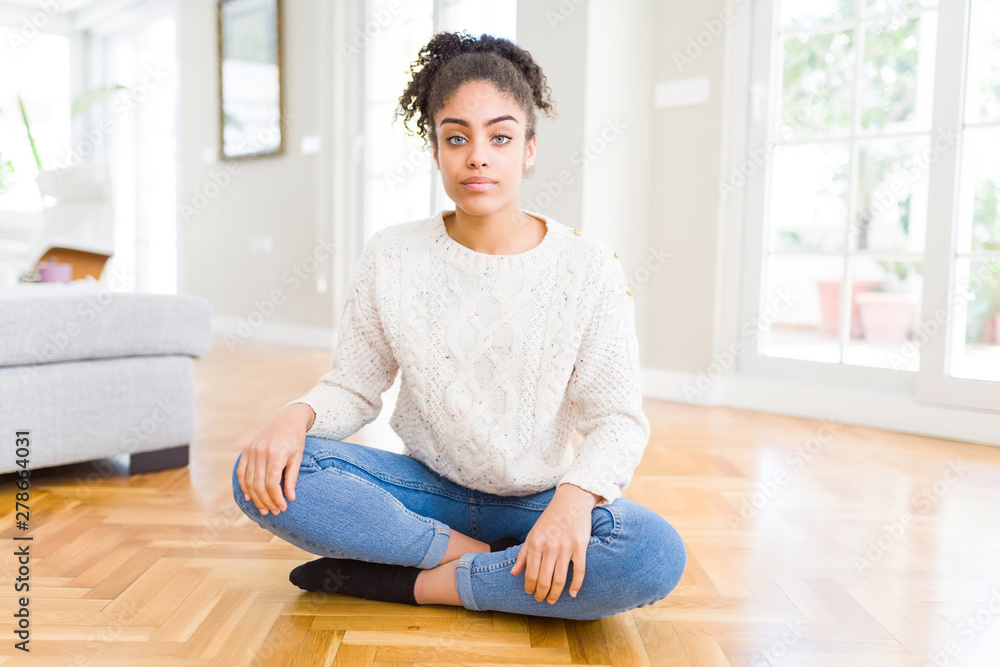 Beautiful young african american woman with afro hair sitting on the floor with serious expression on face. Simple and natural looking at the camera. Beautiful young african american woman with afro hair sitting on the floor with serious expression on face. Simple and natural looking at the camera.