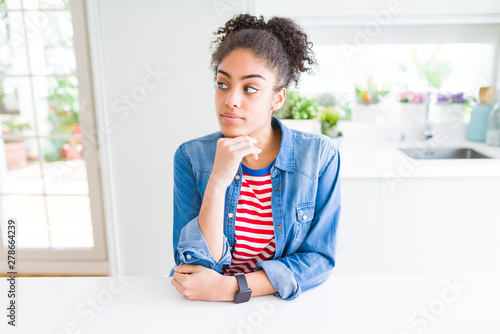 Beautiful young african american woman with afro hair wearing casual denim jacket with hand on chin thinking about question  pensive expression. Smiling with thoughtful face. Doubt concept.