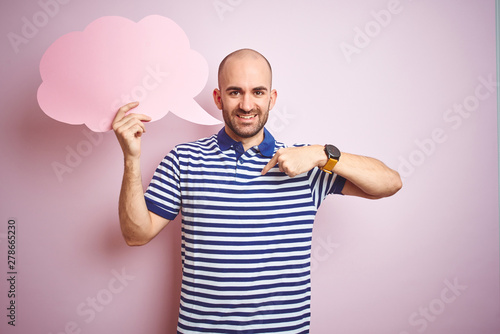 Young man holding speech bubble with blank space for message over pink isolated background with surprise face pointing finger to himself