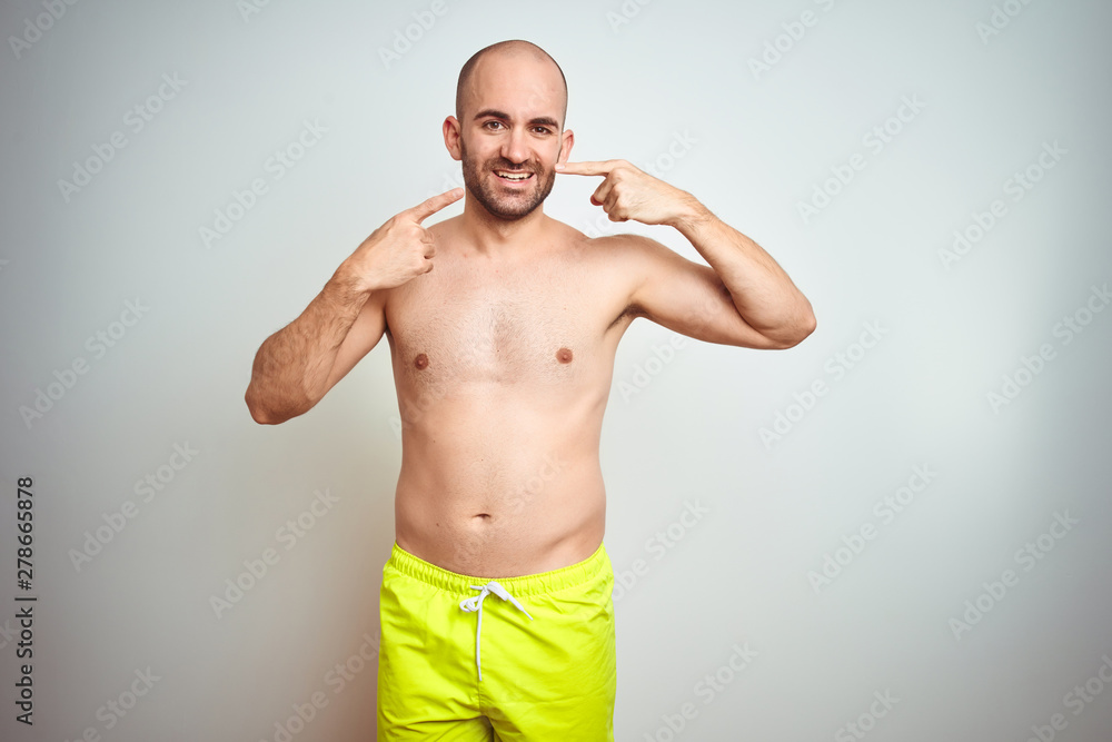 Fototapeta premium Young shirtless man on vacation wearing yellow swimwear over isolated background smiling cheerful showing and pointing with fingers teeth and mouth. Dental health concept.
