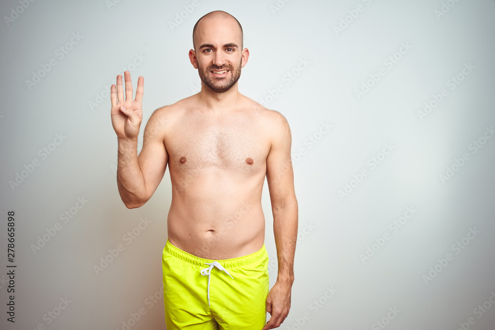 Fototapeta premium Young shirtless man on vacation wearing yellow swimwear over isolated background showing and pointing up with fingers number four while smiling confident and happy.