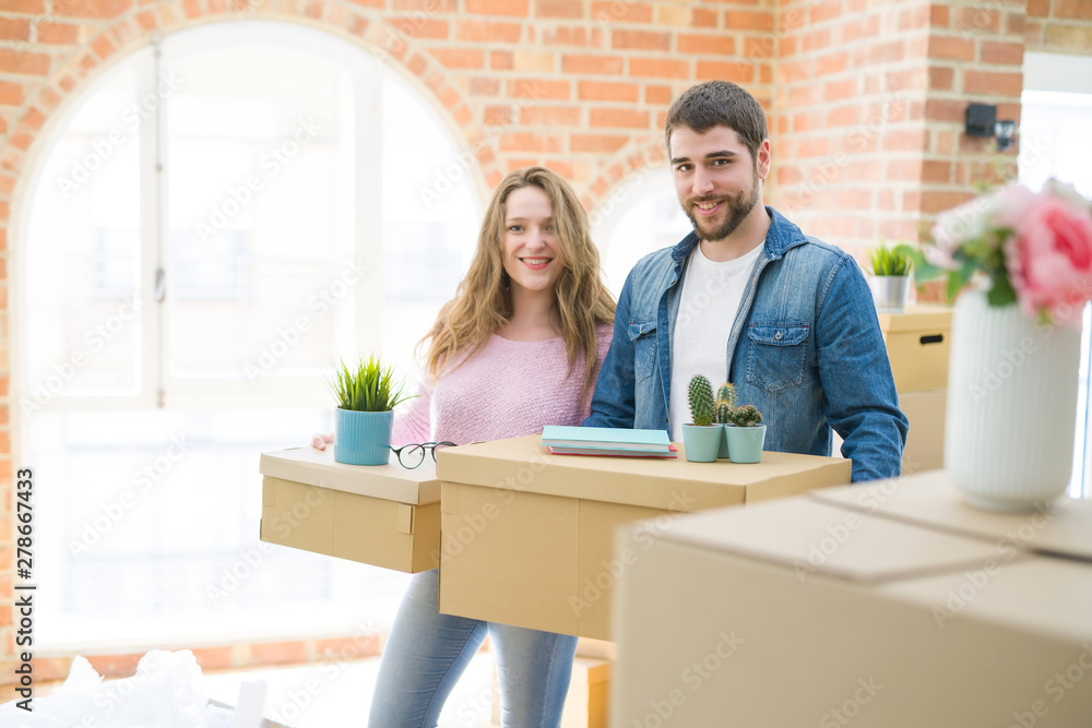 Fototapeta premium Young beautiful couple very happy together holding cardboard boxes moving to a new home