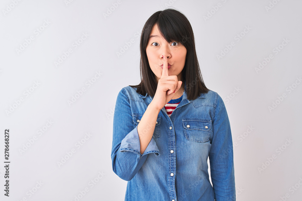 Young beautiful chinese woman wearing denim shirt over isolated white background asking to be quiet with finger on lips. Silence and secret concept. Young beautiful chinese woman wearing denim shirt over isolated white background asking to be quiet with finger on lips. Silence and secret concept.