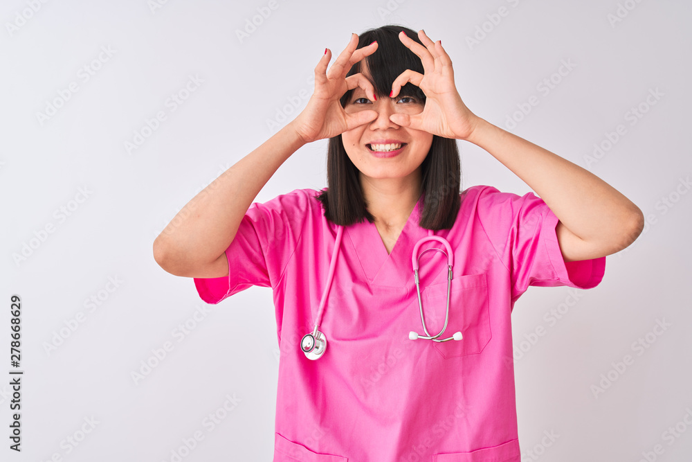Young beautiful Chinese nurse woman wearing stethoscope over isolated white background doing ok gesture like binoculars sticking tongue out, eyes looking through fingers. Crazy expression. Young beautiful Chinese nurse woman wearing stethoscope over isolated white background doing ok gesture like binoculars sticking tongue out, eyes looking through fingers. Crazy expression.