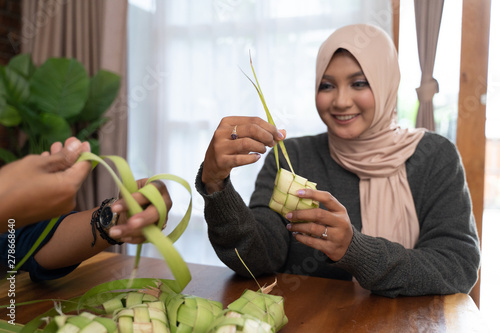 Two veiled woman hold coconut leaves learning how to make a woven wrapper of ketupat