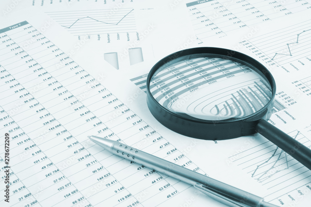 Business concept, magnifying glass and pen on financial charts and graphs Business concept, magnifying glass and pen on financial charts and graphs