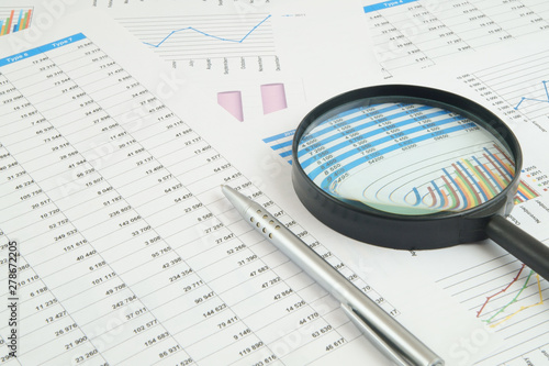 Business concept, magnifying glass and pen on financial charts and graphs