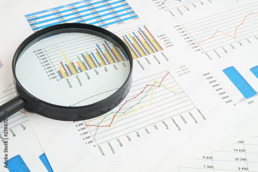 Business concept, magnifying glass on financial charts and graphs Business concept, magnifying glass on financial charts and graphs