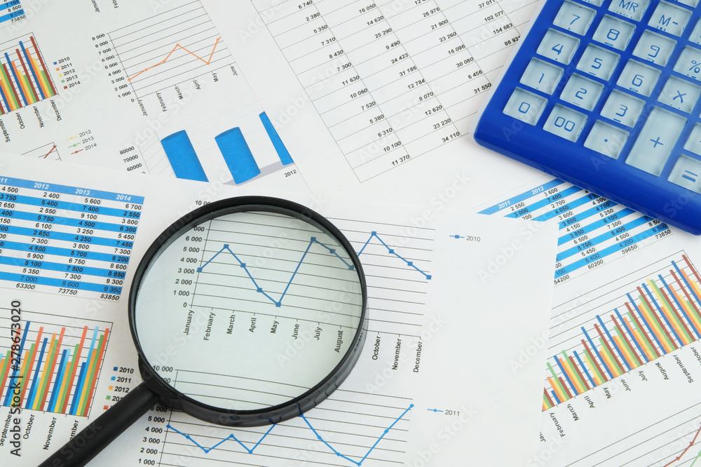 Business concept, calculator and magnifying glass on financial charts and graphs Business concept, calculator and magnifying glass on financial charts and graphs