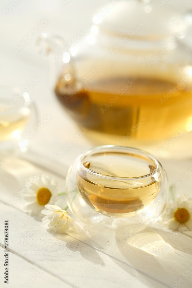 Chamomile tea.Organic natural chamomile tea in a transparent glass teapot and cups, chamomile flowers on a white wooden table.Herbal Green Teas Chamomile tea.Organic natural chamomile tea in a transparent glass teapot and cups, chamomile flowers on a white wooden table.Herbal Green Teas