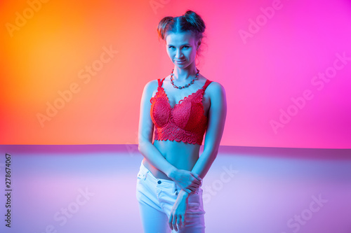 Cinematic night portrait of woman in neon. High Fashion model girl in colorful bright neon lights posing in studio, portrait of beautiful woman in top and jeans.