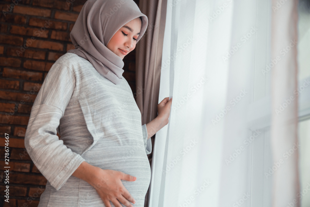 beautiful asian woman pregnant wearing hijab standing next to window beautiful asian woman pregnant wearing hijab standing next to window