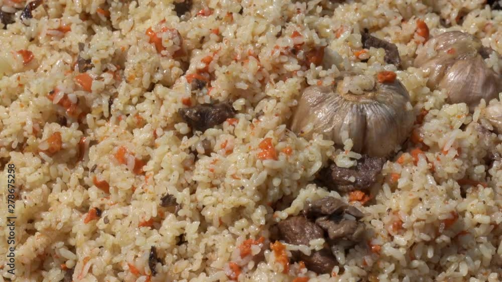 Cooking pilaf in cauldron and mixing pilaf holding kitchen spoon. National Eastern tasty food. Asian traditional culinary dish - pilaf. Ingredients: rice with meat, fat and vegetables, spices. Cooking pilaf in cauldron and mixing pilaf holding kitchen spoon. National Eastern tasty food. Asian traditional culinary dish - pilaf. Ingredients: rice with meat, fat and vegetables, spices.