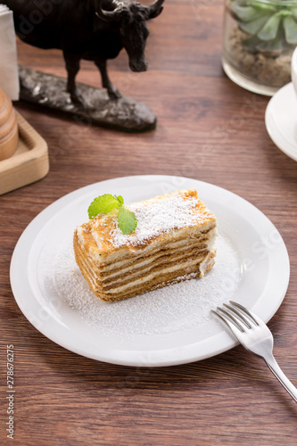 Fototapeta Naklejka Na Ścianę i Meble -  Slice of layered honey cake with mint leaves on wooden table
