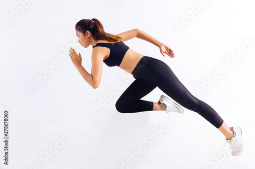 Side view of slim Asian female in black sportswear sprinting fast during workout against white background