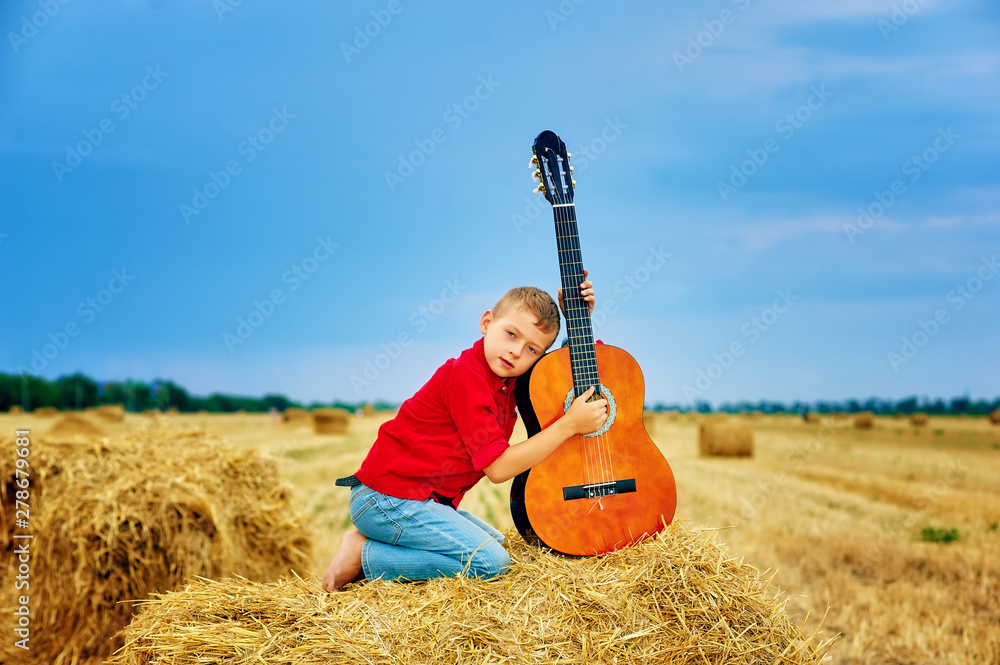 Romantic boy with a guitar in the field . fashionable little musician in nature . children's music education Romantic boy with a guitar in the field . fashionable little musician in nature . children's music education