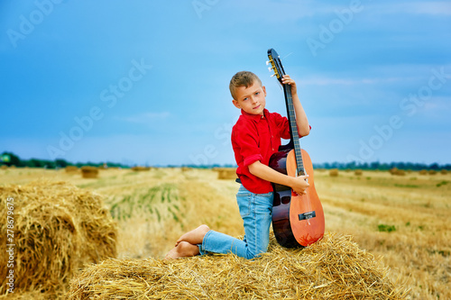 Romantic boy with a guitar in the field . fashionable little musician in nature . children's music education