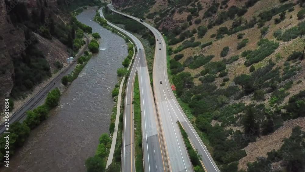 Aerial, drone shot, tilting over traffic on Interstate 70 and the Colorado river, between steep mountain walls, on a partly sunny, summer day, in USA Aerial, drone shot, tilting over traffic on Interstate 70 and the Colorado river, between steep mountain walls, on a partly sunny, summer day, in USA