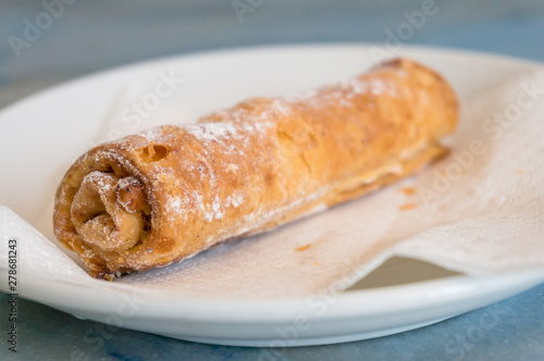 Sweet pastry roll with sugar powder on white plate