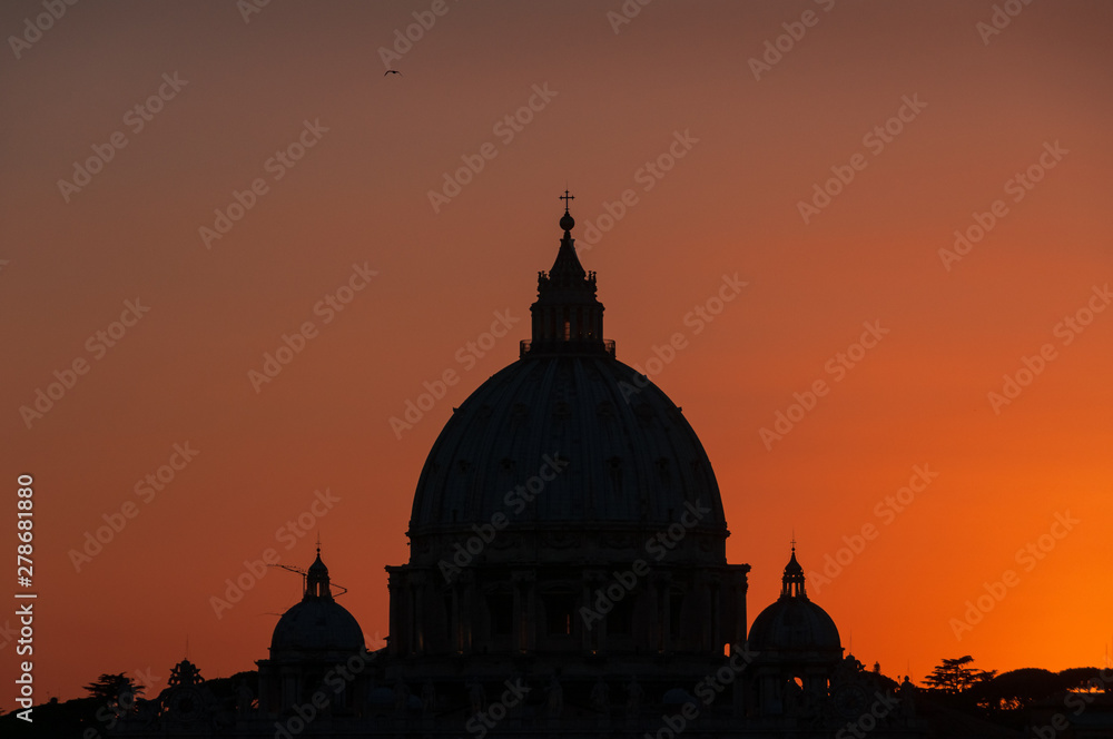 Dark silhouette of the dome of St Peters Basilica against bright red sunset sky