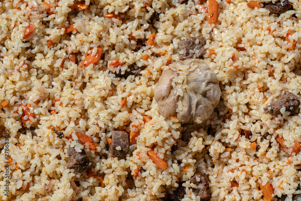 Traditional Eastern culinary dish - pilaf. Ingredients: rice with slices of meat, fat and vegetables (carrot, garlic), spices - popular recipe. Close-up view of Asian tasty food background. Traditional Eastern culinary dish - pilaf. Ingredients: rice with slices of meat, fat and vegetables (carrot, garlic), spices - popular recipe. Close-up view of Asian tasty food background.
