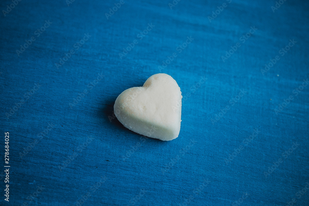 Obraz premium Heart on a blue background. White candy in the shape of a heart on a wooden background.