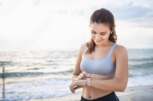 Pretty young brunette woman in a sportswear checking pulse after workout near the sea shore at sunrise. © ianachyrva
