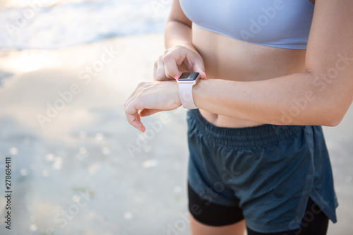 Pretty young woman in a sportswear checking pulse after workout near the sea shore at sunrise.