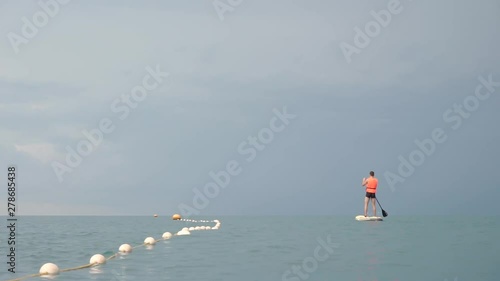 Young guy during vacation rides on sup surfing in the sea. Teen in a life jacket goes surfing.