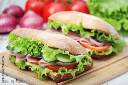 Two sandwiches with fresh vegetables, ham and cheese in ciabatta bread